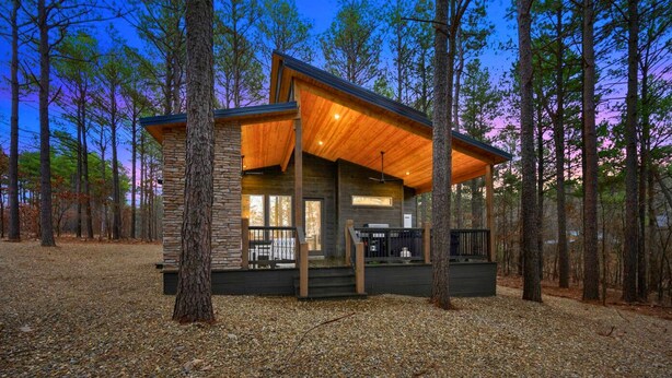 A cabin with a wooden exterior, large windows, and a covered porch area. - Secluded Forest Retreat with Game Lounge (Broken Bow)