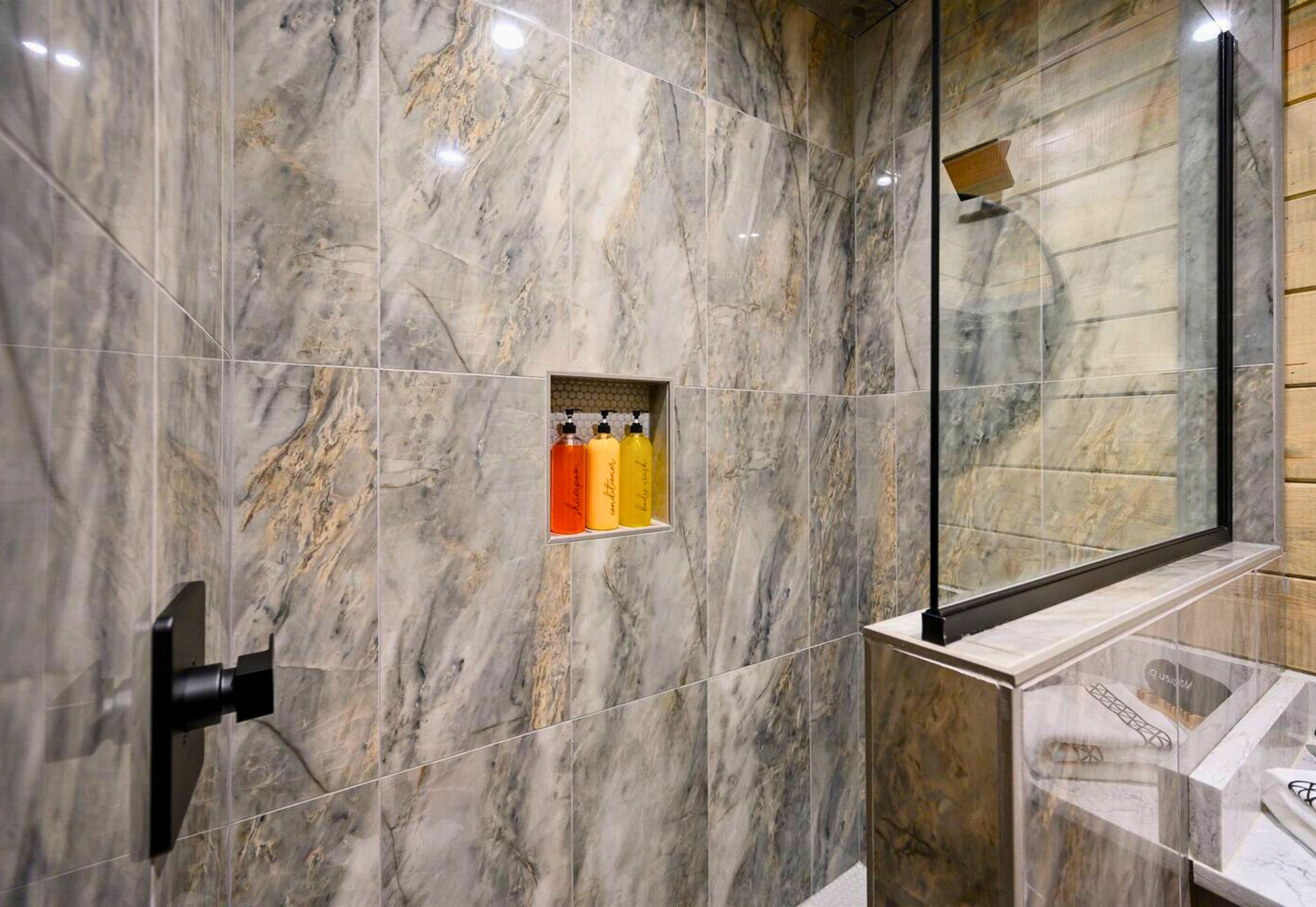 Ein Badezimmer mit Marmorfliesen, einer Duschkabine aus Glas und einem Ablagebereich für Pflegeprodukte.