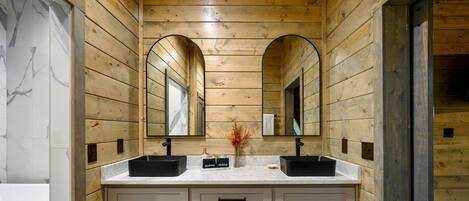 A wooden bathroom with two sinks, a mirror, and a vase with flowers.