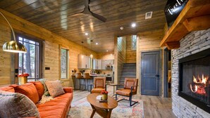 A cozy cabin interior with a fireplace, wooden walls, a sofa, and a kitchen area. - Secluded Forest Retreat with Game Lounge (Broken Bow)