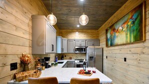 A modern kitchen with wooden walls, white cabinets, stainless steel appliances, and a large island with seating. - Secluded Forest Retreat with Game Lounge (Broken Bow)