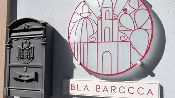 Un buzón y un letrero circular con una ilustración de un edificio y el nombre "BLA BAROCCA".