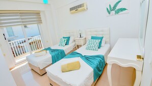 Hotellihuone, jossa on kaksi sänkyä, pieni yöpöytä lampun kanssa, suuri ikkuna sälekaihtimilla ja parveke.