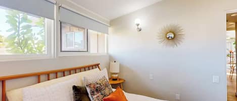 A bedroom with a bed, pillows, a nightstand, a lamp, and a wall-mounted light fixture.
