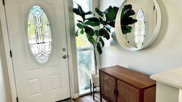 A white door with a stained glass window, a potted plant, a round mirror, and a wooden cabinet.