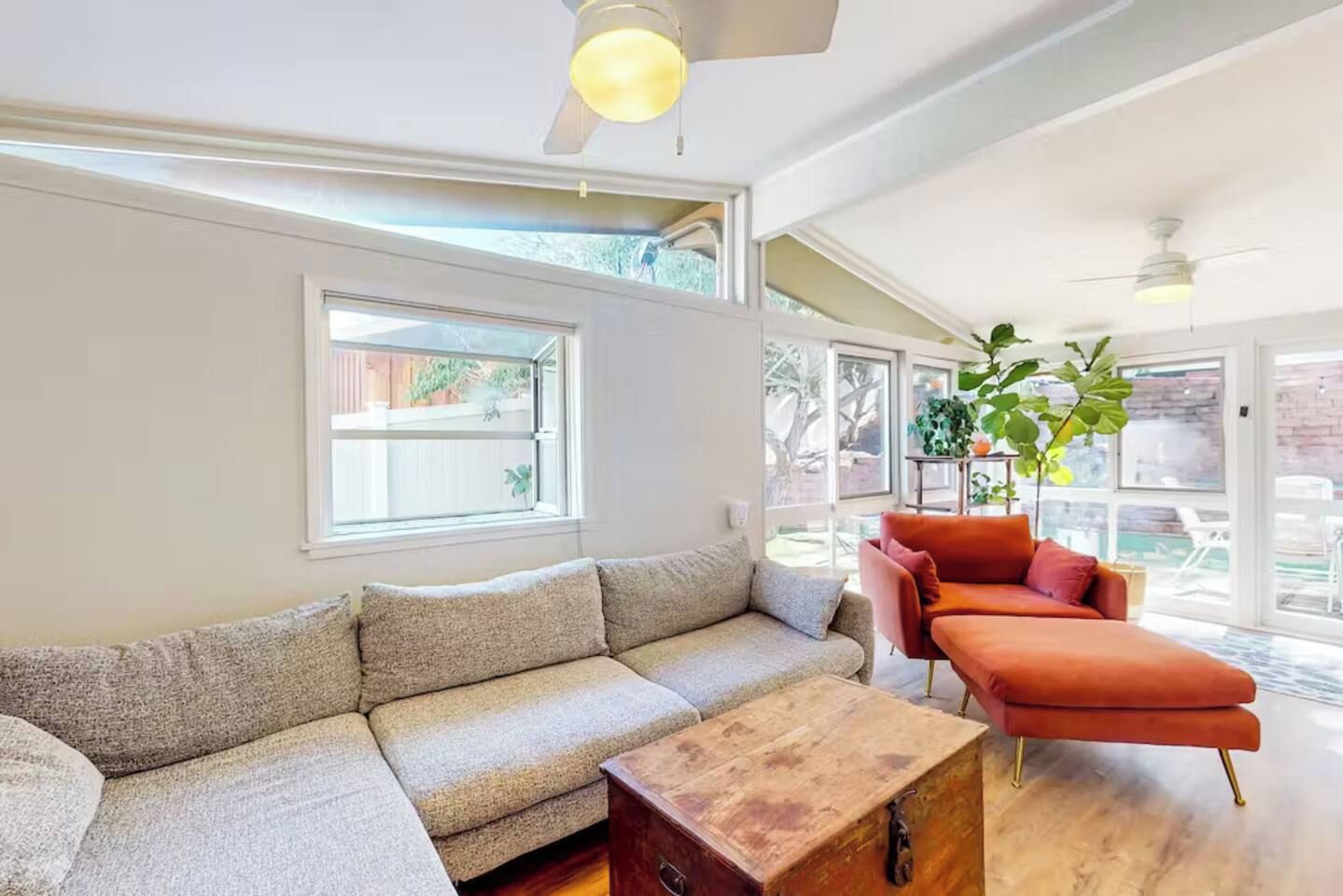 Ein Wohnzimmer mit einem Ecksofa, einem roten Sessel, einem Holztisch und einem Deckenventilator.