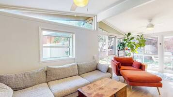 Ein Wohnzimmer mit einem Ecksofa, einem roten Sessel, einem Holztisch und einem Deckenventilator.