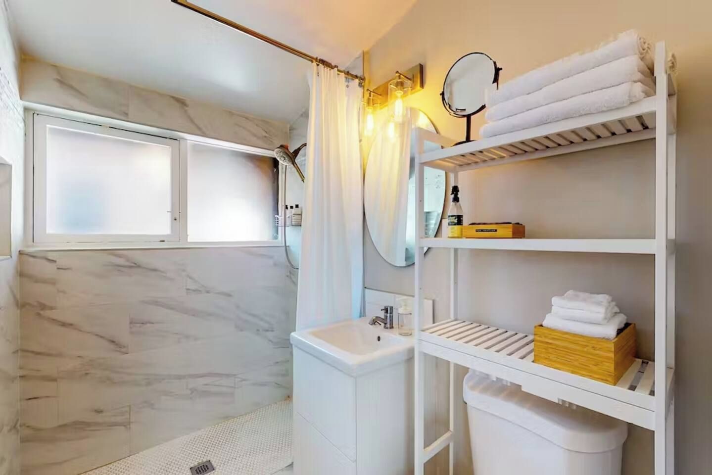 Ein Badezimmer mit Dusche, Waschbecken, Spiegel und Regalen mit Handtüchern.