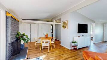 A spacious living area with a fireplace, a dining table, and a television mounted on the wall.