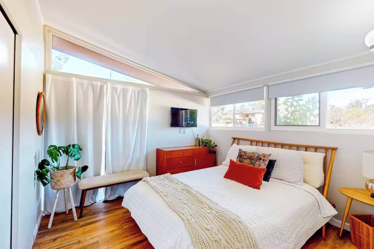 A bedroom with a bed, a bench, a TV, and a window.