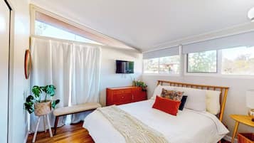 A bedroom with a bed, a bench, a TV, and a window.