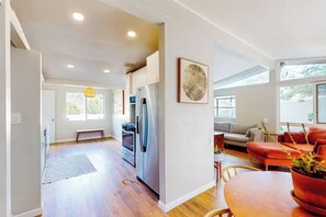 A modern kitchen with a refrigerator, oven, and dining area with a table and chairs. - Mid-Century Treehouse with Yard and Views! AMAZING Location! Pet-friendly! (Spring Valley)