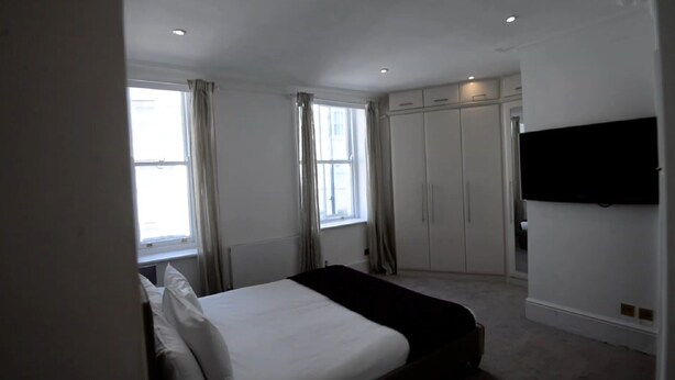 A bedroom with a bed, a wardrobe, a TV, and a window with curtains. - Beautiful 2-bed Flat in London (London)