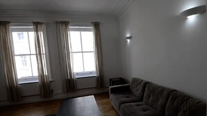 A living room with a sofa, a coffee table, and two windows with curtains. - Beautiful 2-bed Flat in London (London)