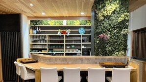 A bar area with a counter, white chairs, and shelves with various items.