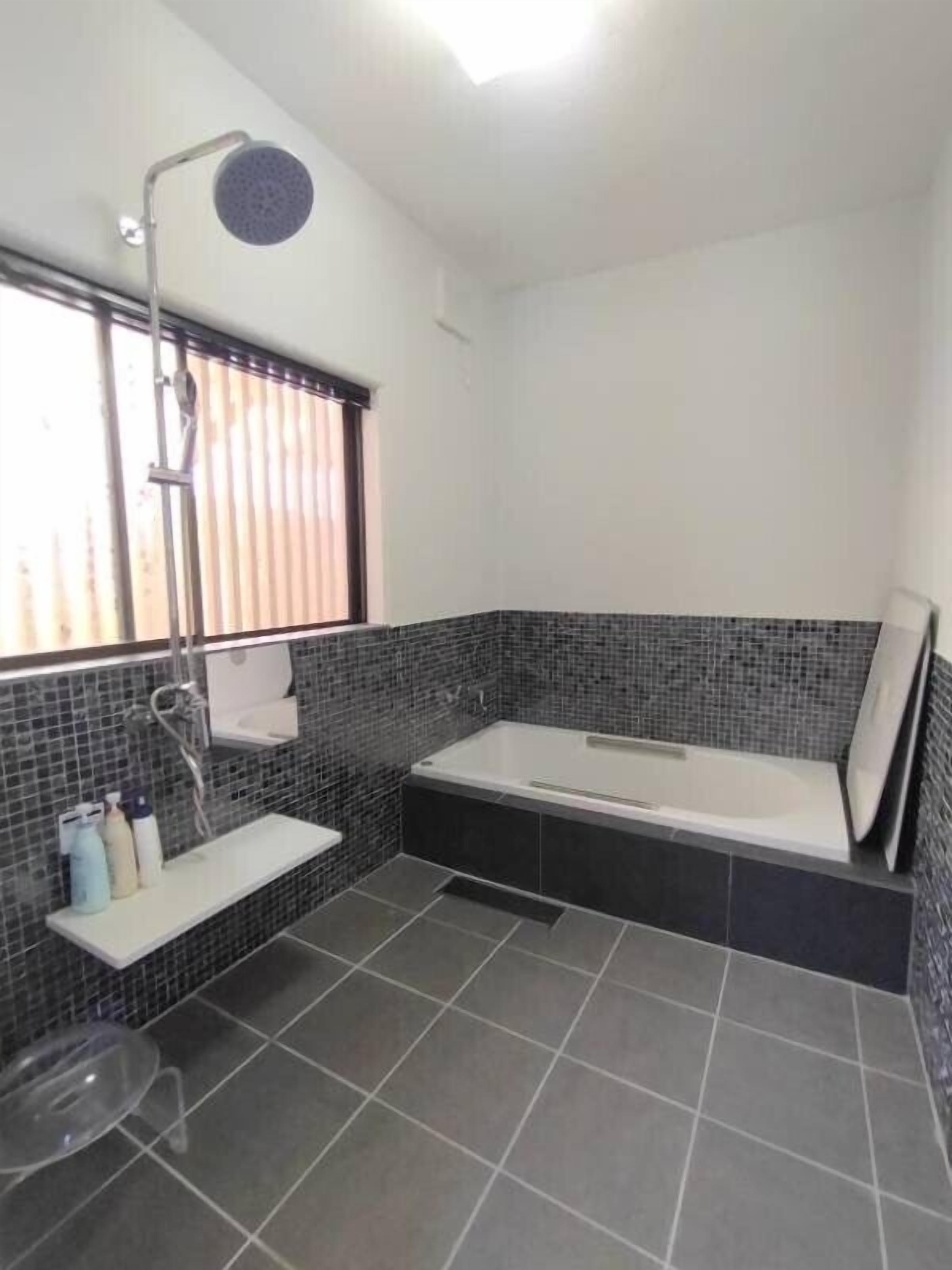 A modern bathroom with a bathtub, a shower, and a window with blinds.