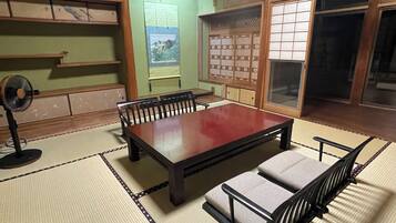 A traditional tatami mat room with a low table and benches, a fan, and shoji screens.