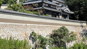 A traditional Japanese building with a tiled roof and a stone wall in the foreground.