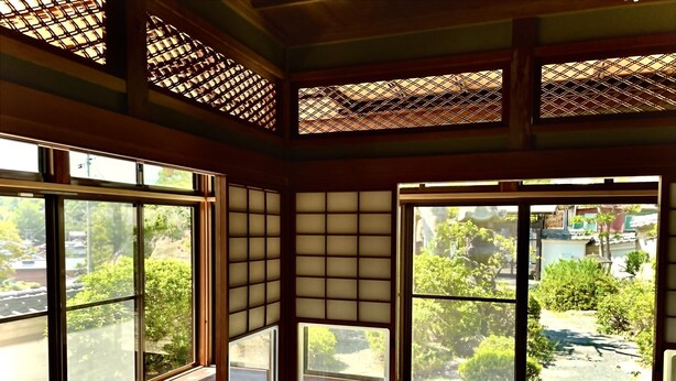 A room with large windows, tatami mats, and a view of greenery and buildings.