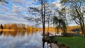 A serene lakeside scene with a dock, grassy banks, and trees reflecting on the water. - Comfortable vacation apartment Senzig, 150 m to the beach (Königs Wusterhausen)