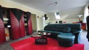 A modern living room with a sectional sofa, a red rug, and a bookshelf. - Comfortable vacation apartment Senzig, 150 m to the beach (Königs Wusterhausen)
