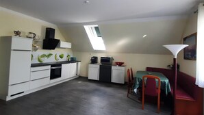 A compact kitchen with white cabinets, a dining area with a red sofa, and a small table. - Comfortable vacation apartment Senzig, 150 m to the beach (Königs Wusterhausen)