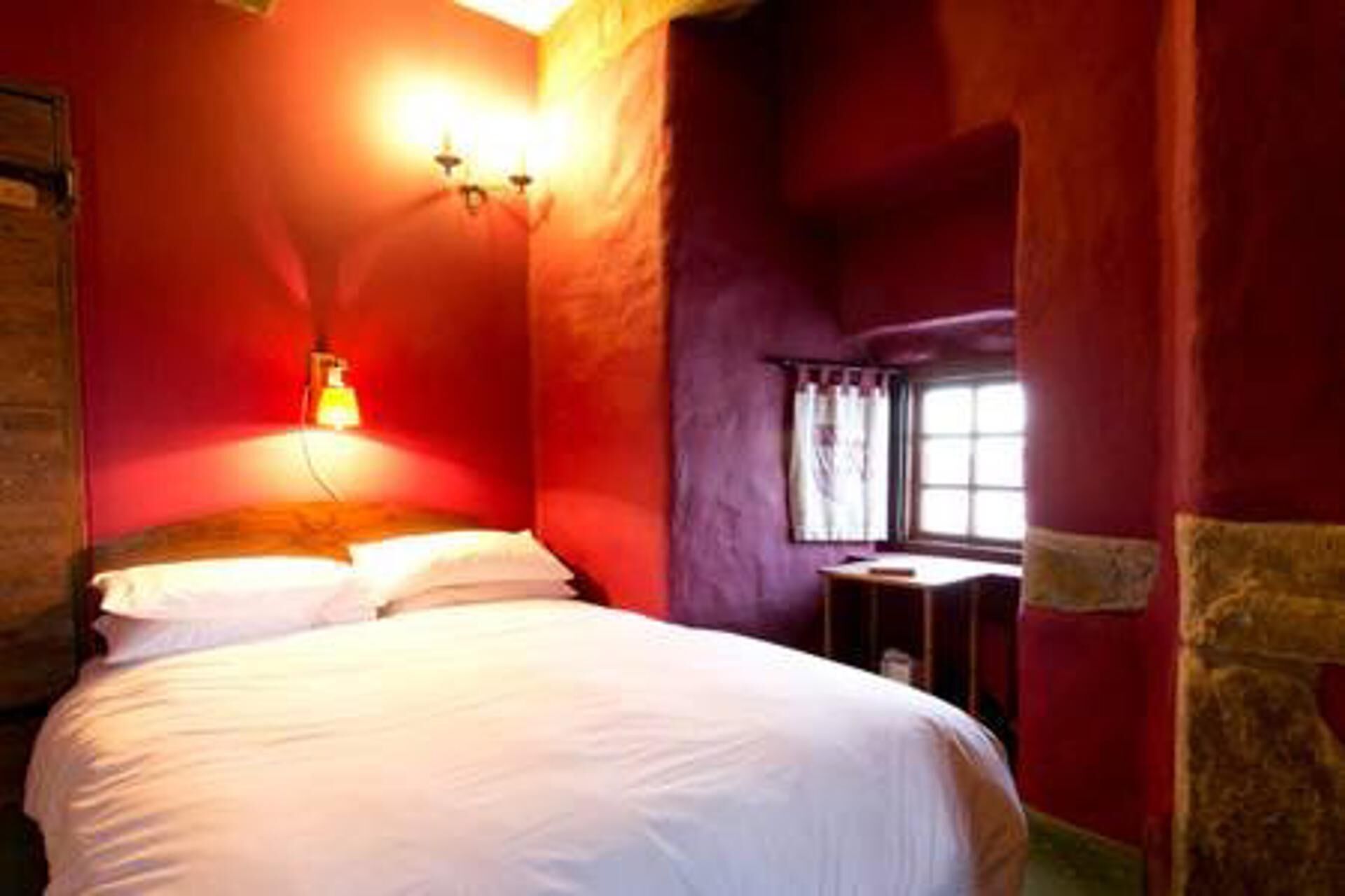 A room with a bed, a nightstand, a lamp, and a window.