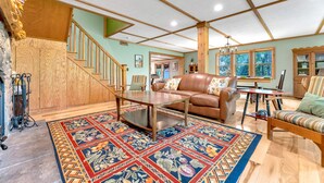 A spacious living room with a wooden staircase, a leather sofa, a coffee table, and a patterned rug. - Peaceful Lakefront Cabin Retreat with Hot Tub! (Deerfield)