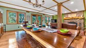 A spacious dining area with a long wooden table, benches, and a stone fireplace. - Peaceful Lakefront Cabin Retreat with Hot Tub! (Deerfield)