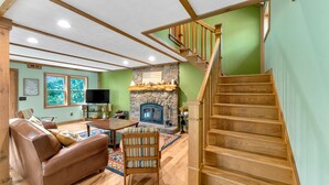 A living room with a stone fireplace, wooden staircase, and a leather sofa. - Peaceful Lakefront Cabin Retreat with Hot Tub! (Deerfield)