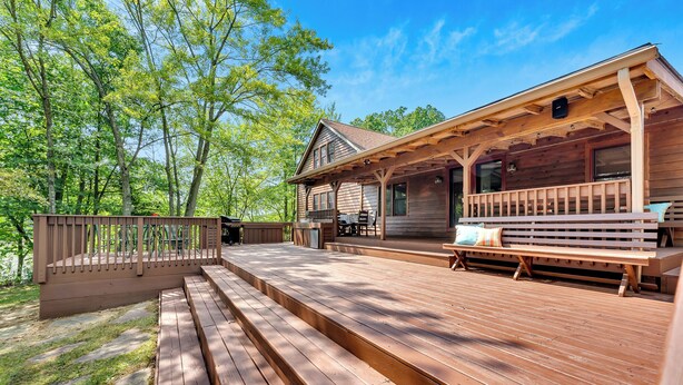 A wooden deck with a covered porch, outdoor seating, and a stone pathway. - Peaceful Lakefront Cabin Retreat with Hot Tub! (Deerfield)