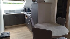 A compact kitchen with a sink, stove, and microwave. There's a dining area with a table and chairs. - La Chèvrerie (Taintrux)