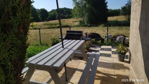 A patio area with a wooden table and bench, an umbrella, and a view of a fenced field with animals. - La Chèvrerie (Taintrux)