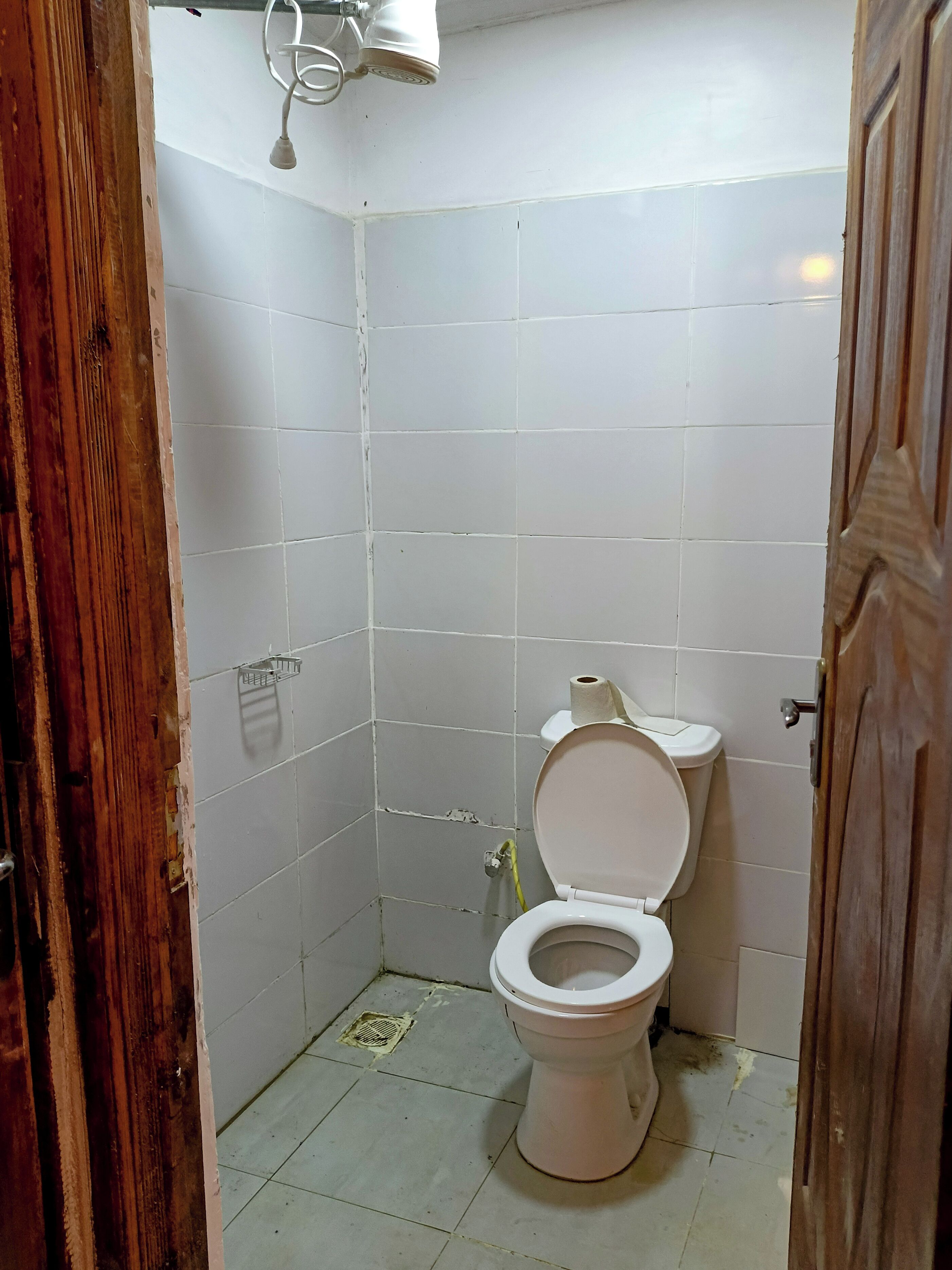 Een kleine, eenvoudige badkamer met toilet, douchekop en betegelde wanden.