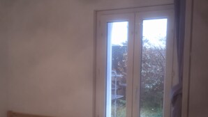 A bedroom with a single bed, a window with a view of greenery, and a door. - T3 Avec Jardin (Agde)