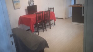A dining area with a red tablecloth, wooden chairs, a television, and a painting on the wall. - T3 Avec Jardin (Agde)