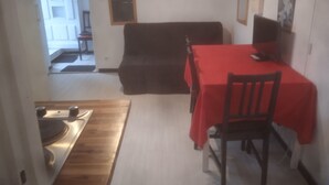 A dining area with a table covered in a red tablecloth, a dark sofa, and a chair. - T3 Avec Jardin (Agde)