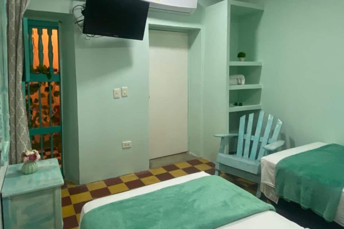 A room with two beds, a TV mounted on the wall, a small table with a vase, and a checkered floor.