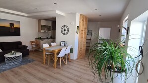 Un salon moderne comprenant un coin repas, un plancher en bois, un canapé noir, une table basse ronde et une grande plante en pot.