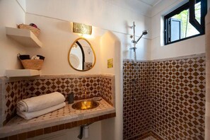 A bathroom with a sink, mirror, and shower. There are baskets on a shelf and a towel on the counter. - Riad Familial Privatisé au Calme Avec vue sur Marrakech (Marrakech)