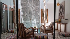 A cozy living room with patterned rugs, wooden furniture, and a large window with patterned curtains. - Riad Familial Privatisé au Calme Avec vue sur Marrakech (Marrakech)
