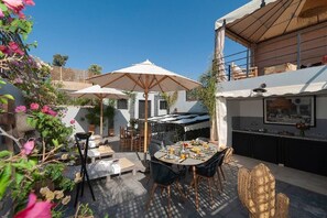 An outdoor dining area with tables and chairs, umbrellas, and a view of the surrounding buildings. - Riad Familial Privatisé au Calme Avec vue sur Marrakech (Marrakech)