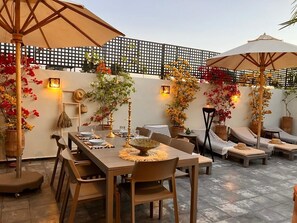 An outdoor patio with a dining table set for four, surrounded by lounge chairs and umbrellas. - Riad Familial Privatisé au Calme Avec vue sur Marrakech (Marrakech)