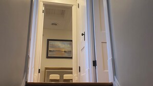 Una escalera de madera que conduce a una habitación con una lámpara en el techo, una puerta y un cuadro en la pared.
