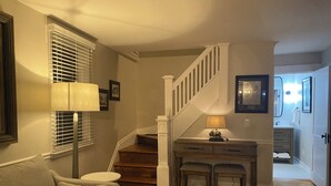 Una sala de estar con sofá, lámpara, escalera y escritorio con cajones.