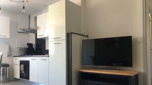 Una cocina moderna con armarios blancos, encimera negra y horno empotrado. Un televisor de pantalla plana está montado sobre un atril de madera.