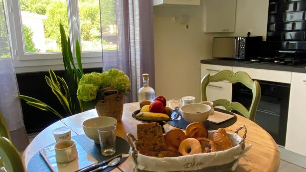 Una mesa de comedor con una cesta de pasteles, un cuenco de fruta y una taza de café.