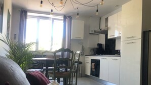 Una cocina moderna con armarios blancos, lavavajillas y encimera negra. Hay una mesa de comedor con sillas y una planta en la esquina.