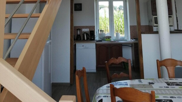 A multi-level interior with a wooden staircase, a dining area with a table and chairs, and a kitchen with appliances. - Gîte du Haut Montbrault (Fleurigné)
