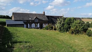 A two-story house with a sloped roof, a visible chimney, and a large grassy yard. - Gîte du Haut Montbrault (Fleurigné)